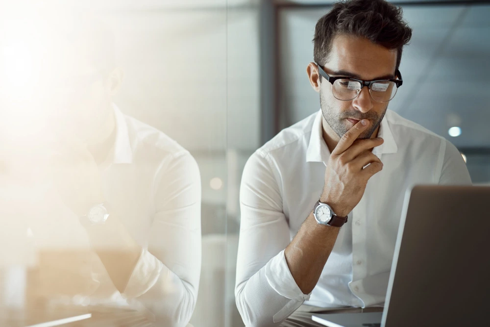 Man with glasses in white shirt working on a laptop